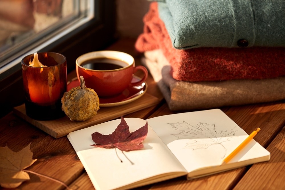 Cozy fall picture with cup of coffee and journal sketch book with leaf and warm sweaters.